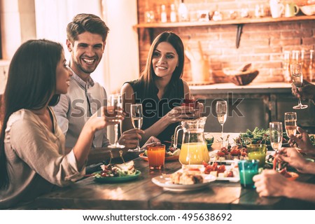 Dinning with friends. Cheerful young people enjoying meal while sitting at the dinning table on the kitchen together