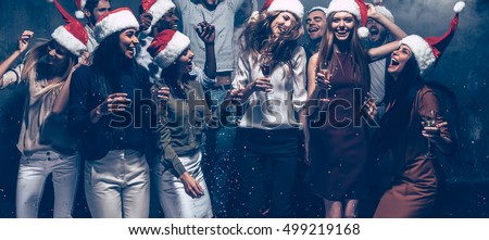 Enjoying New Year party. Group of beautiful young people in Santa hats dancing and looking happy