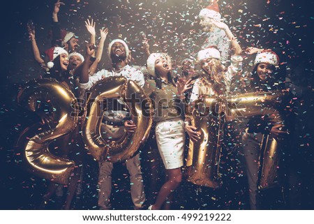 Happy New 2017 Year! Group of cheerful young people in Santa hats carrying gold colored numbers and throwing confetti