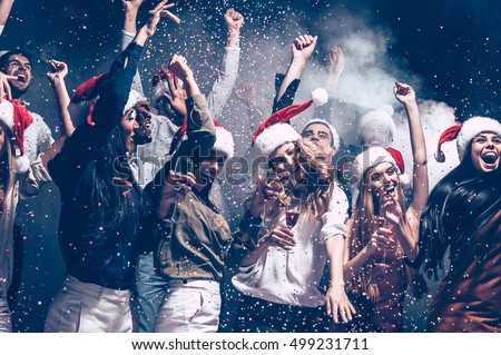 Christmas fun. Group of beautiful young people in Santa hats throwing colorful confetti and looking happy