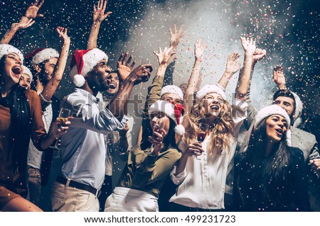 They love Christmas. Group of beautiful young people in Santa hats throwing colorful confetti and looking happy