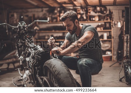 This bike will be perfect. Confident young man repairing motorcycle in repair shop
