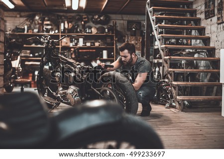 Man repairing bike. Confident young man repairing motorcycle in repair shop