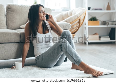 Good talk with boyfriend. Attractive young woman talking on mobile phone and smiling while sitting on the carpet at home