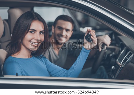 Happy car owners. Beautiful young couple sitting at the front seats of their new car while woman showing keys and smiling