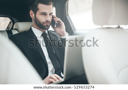 Always available. Handsome young businessman working on his laptop and talking on the phone while sitting in the car
