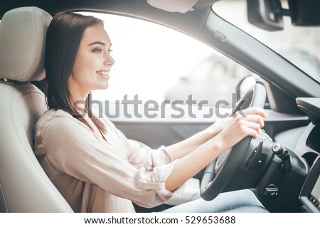 Driving around city. Young attractive woman smiling and looking straight while driving a car