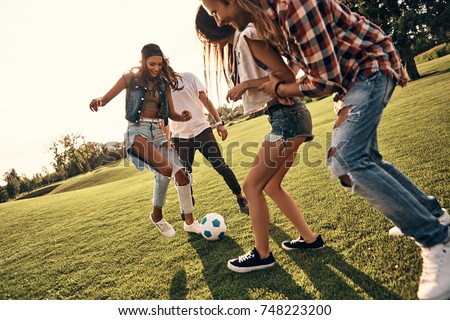 Playful friends. Group of young smiling people in casual wear enjoying nice summer day while playing soccer outdoors