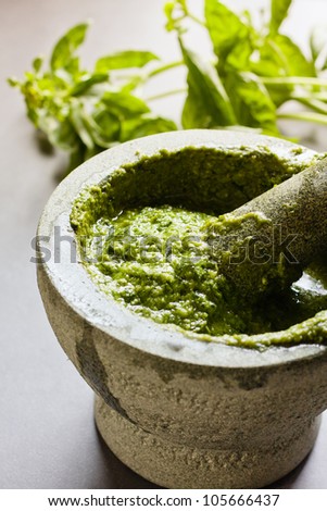 Homemade Pesto in mortar and pestle and basil leaves on yhe background