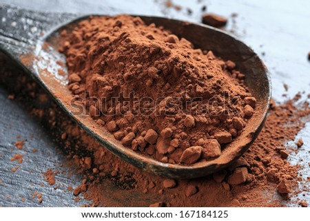 Cocoa powder in a wooden spoon on black background, close-up