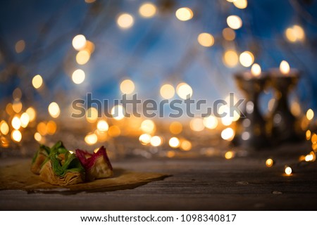 Arabic sweets on a wooden surface. Candle holders, night light and night blue sky with crescent moon in the background.