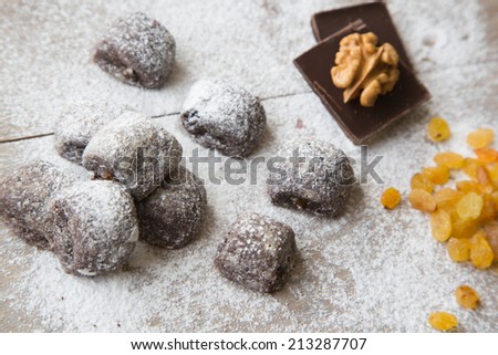 Small chocolate biscuits with raisins and walnuts covered by sugar powder.