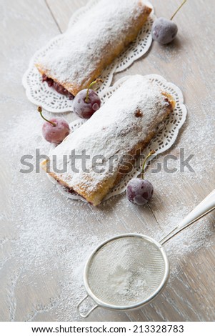Traditional romanian dessert - invertita.Baked rolled thin dough stuffed with sour cherries. Frozen sour cherries and a tea strainer in the background.The dessert placed on the wooden surface.Top view