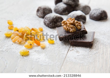 Two pieces of chocolate and a wallnut on it.Small chocolate biscuits with raisins and wallnuts in the background