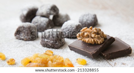 Two pieces of chocolate and a walnut on it.Small chocolate biscuits with raisins and wallnuts in the background