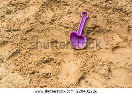 A violet plastic shovel from the children tool set was left in the sandbox