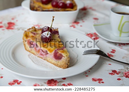 A piece of cherry pie on the white plate. A cherry pie in the ceramic mold and a cup of coffee  in the background