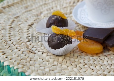 Handmade chocolate truffle with dried apricot on a woven surface. Dried apricots, pieces of chocolate  and a cup of tea in the background