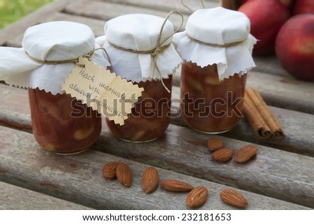 Glasses of homemade peach marmalade with almond nuts and cinnamon on an old wooden surface.Almonds,cinnamon sticks and fresh peaches in the background