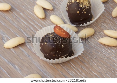 Handmade chocolate truffle with almond nut on the wooden surface. Peeled almonds in the background