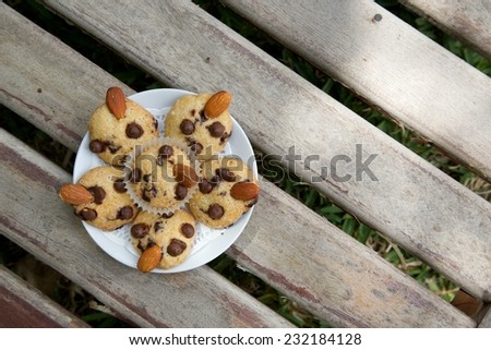 A plate of mini shortcakes with chocolate chips and almond nuts on the wooden surface. Free space for a text.Top view