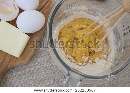 Mixed ingredients in the glass measuring cup for preparing biscuits . Eggs and butter in the background