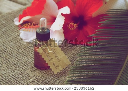 A dropper bottle of hibiscus essential oil. Flowers of hibiscus in the background