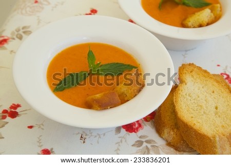 Light lunch soup-tomato soup with croutons in white plates on a flower print table cloth