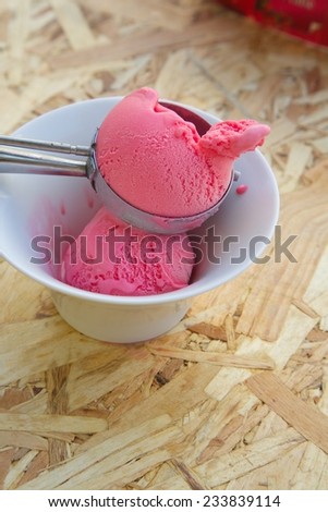 Red berries ice cream in a white plate and a ice-cream spoon on the wooden surface. Close up