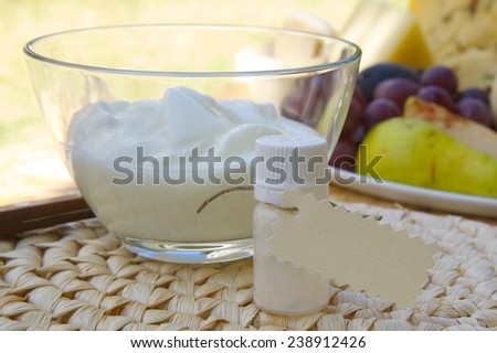 Dried yogurt starter in the small plastic bottle with a label. Prepared yogurt and fresh fruits in the background. Free space for a text
