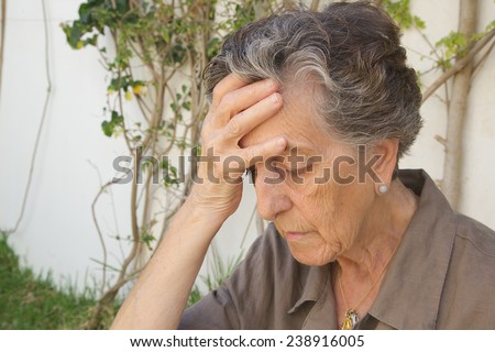 An old woman between 70 and 80 shows that she has a strong headache touching her forehead with a hand
