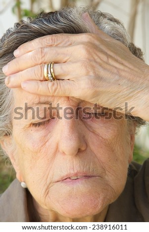 An old woman between 70 and 80 years old is touching her forehead with her hand showing that she has a strong headache.
