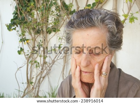 An old woman between 70 and 80 years old is touching her face with both hands expressing her preoccupation