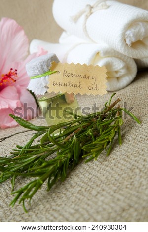 A bottle of rosemary essential oil on a sackcloth. Rosemary twigs and hibiscus flowers in the background