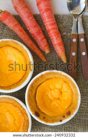 Homemade carrot cheese cakes in white ceramic moulds. Carrots and dessert spoons on a sackcloth. Top view