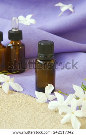 A dropper bottle of jasmine essential oil. Jasmine blossoms in the background