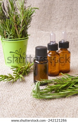 A dropper bottle of rosemary essential oil. Rosemary twigs in a green decorative bucket in the background.