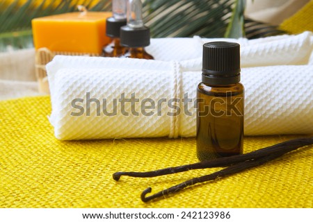 A dropper bottle of vanilla essential oil. Vanilla sticks and white towels in the background.