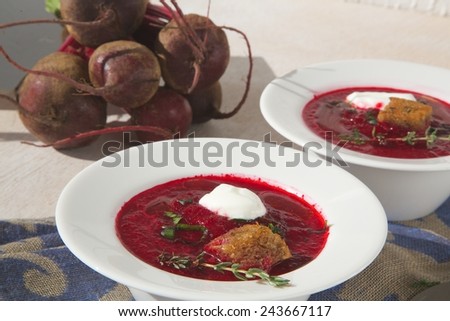 Healthy winter vitamin lunch: red beet root cream soup with fresh parsley,yogurt,thyme and black bread croutons. Fresh red beet roots in the background.