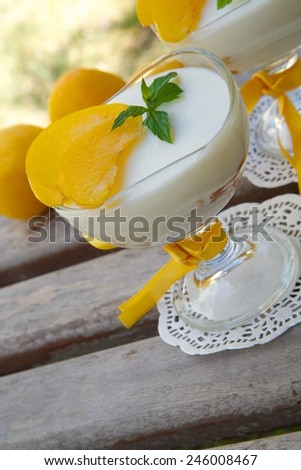 Milk dessert - sweet ricotta cheese with yellow plums in a glass dessert bowl on a wooden surface. Fresh plums in the background.