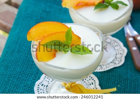 Milk dessert - sweet ricotta cheese with peach in a glass dessert bowl. Dessert spoons with wooden handles in a background.