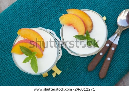 Milk dessert - sweet ricotta cheese with peach in a glass dessert bowl. Dessert spoons with wooden handles in a background.