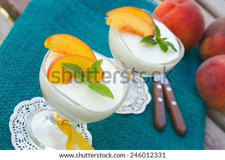 Milk dessert - sweet ricotta cheese with peach in a glass dessert bowl. Dessert spoons with wooden handles and fresh peaches in a background.