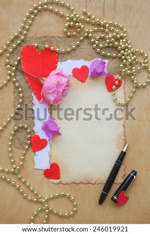 Valentines Day background. Old paper,pink rose,red hearts,violet flowers,black pen,golden perl chain on a wooden surface. Free space for a text
