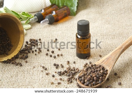 A dropper bottle of black pepper essential oil. Black pepper in the background.