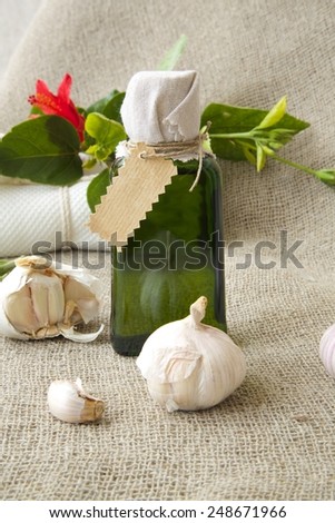 A glass bottle of garlic oil. Cloves of garlic in the background