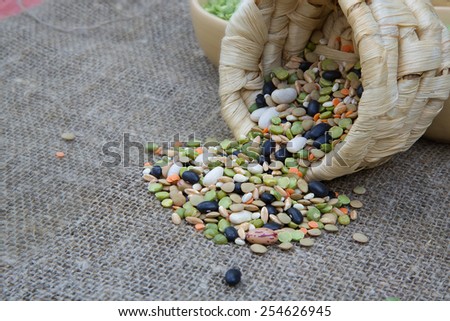 An assortment of dried legumes and cereals: wheat grains, green peas, French beans,pearl barley, orange lentils on a grey sackcloth