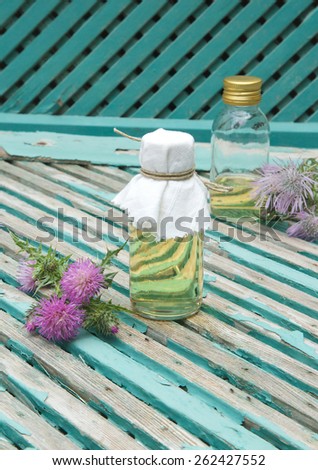 A glass bottle of milk thistle oil. Milk thistle blossoms in the background