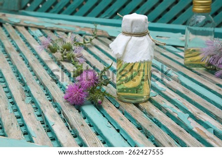 A glass bottle of milk thistle oil. Milk thistle blossoms in the background