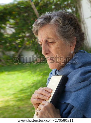 An old woman between 70 and 80 years old put the book close to her heart after having read it. Garden background